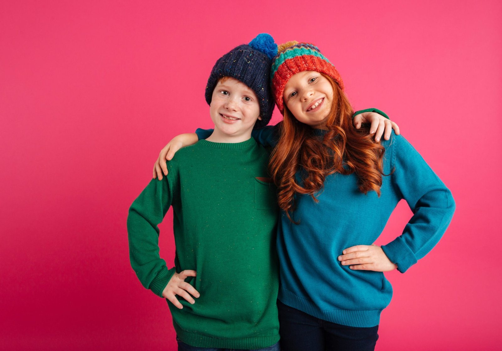Photo of two happy little children isolated over pink background wearing warm hats. Looking camera.